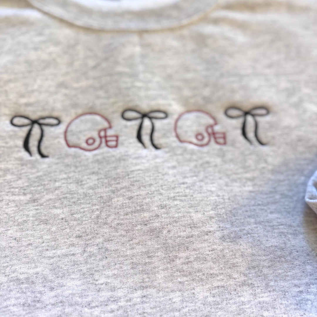 Embroidered football helmet sweatshirt with bow details in a cute coquette gameday style on a cozy crewneck