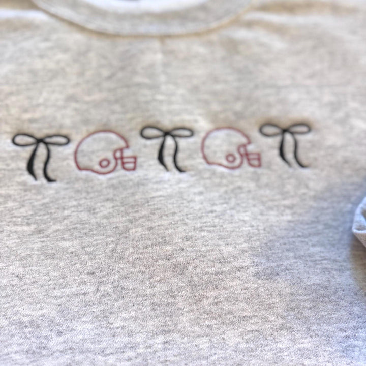 Embroidered football helmet sweatshirt with bow details in a cute coquette gameday style on a cozy crewneck