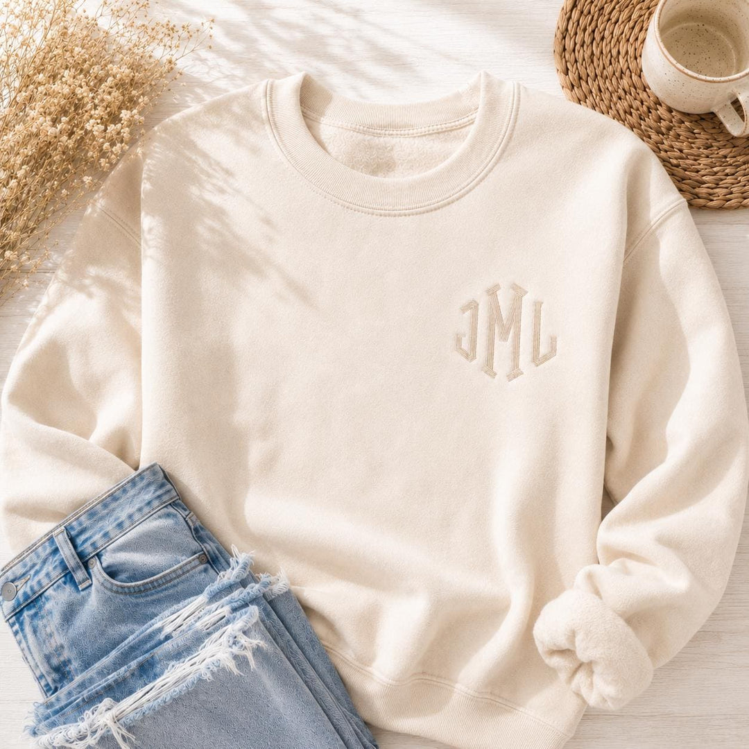 Cream monogrammed sweatshirt with small tone on tone embroidered initials on the left chest, styled in a bright natural light flatlay with jeans.