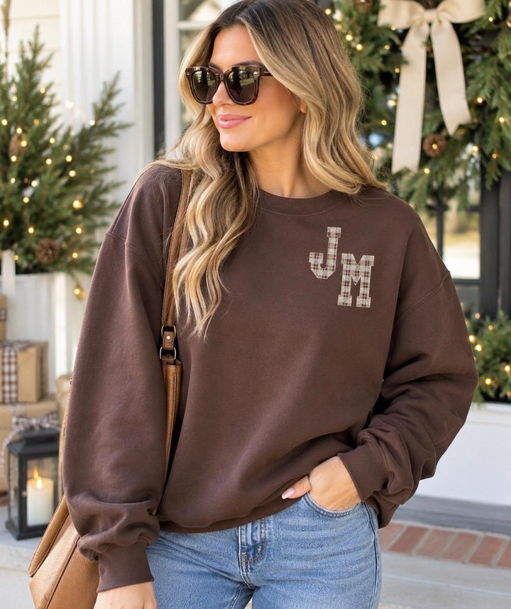 Woman wearing a personalized plaid monogram sweatshirt with embroidered initials, styled with jeans in a bright preppy holiday setting.
